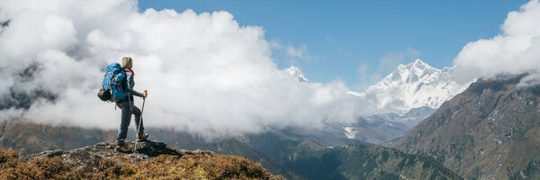 Young hiker backpacker woman using trekking poles enjoying the Nuptse 7861m mountain during high altitude Acclimatization walk. Everest Base Camp trekking route, Nepal. Active vacations concept image