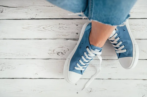 白い木製の床の上にカジュアルな青の新しいスニーカーでティーンエイジャーの足をイメージを閉じます 現代のファッション世界のコンセプトイメージのヴィンテージスタイル — ストック写真