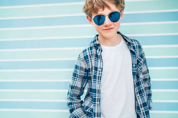 白亜のブロンドの髪のファッションの肖像12歳の10代の男の子は 青のサングラスでチェッカーシャツと白のTシャツを着てターコイズブルーの背景の壁の背景 10代のファッションコンセプト — ストック写真