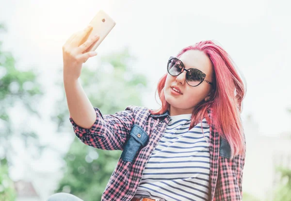 漂亮的现代微笑的少女 有着非凡的发型 穿着格子衬衫 戴着太阳镜 用现代智能手机自拍 青少年的日常生活乐趣与青少年的观念 — 图库照片