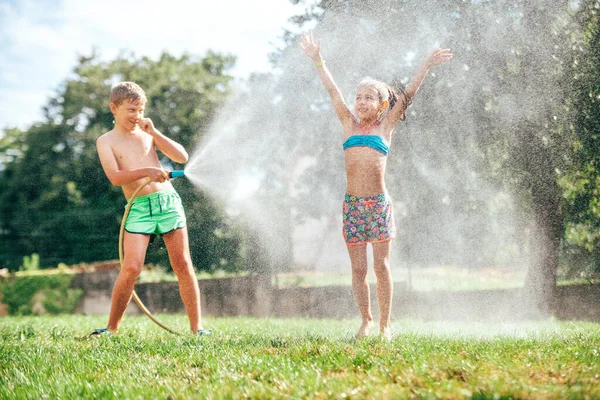 男孩和女孩在花园里玩耍 从软管里相互浇水 制造了一场雨 快乐童年的概念形象 — 图库照片