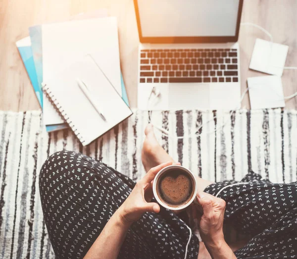 ビジネスの女性は ノートパソコン 紙などでリビングルームのオフィスに座っているハート型の泡で朝のコーヒーを楽しんでパジャマを着ています — ストック写真