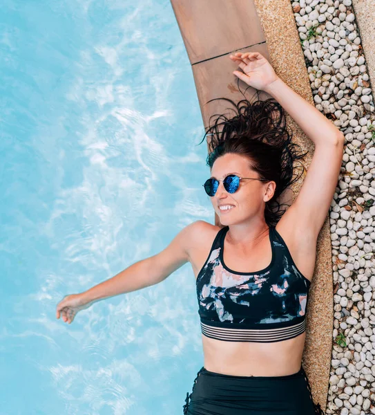 수영장 가장자리에 깨끗하고 파도를 배경으로 포장된 선글라스를 아름다운 미소짓는 — 스톡 사진