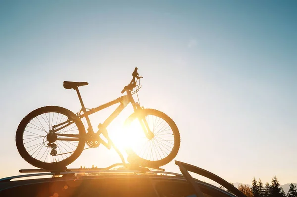 车顶上登着山地自行车的轮廓 背景为晚霞 使用汽车概念图像的安全体育用品运输 — 图库照片