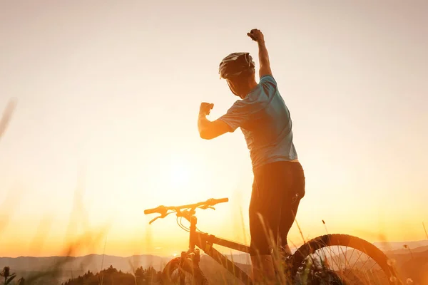 男バイカー男は丘の上で夕日を満たしています 彼は別の成功した日の終わりに片腕の挨拶を上げた アクティブスポーツ人のコンセプトイメージ — ストック写真