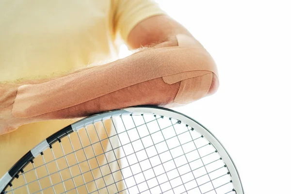 Tennis player elbow taped with elastic therapeutic or Kinesio tape applied on arm lying on racket at orthopedic ward close up image. Active sporty people health rehabilitation concept image.