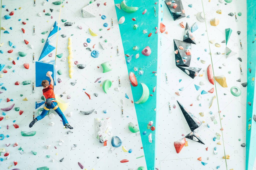 Teenager boy at indoor climbing wall hall. Boy is climbing using an auto belay system and climbing harness. Active teenager time spending concept image.