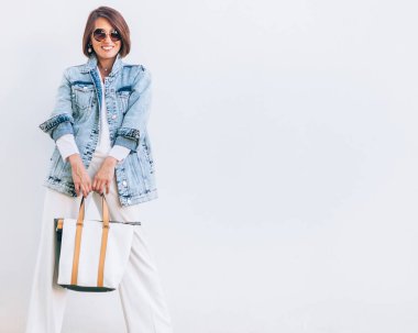 Büyük beden kot ceket ve geniş beyaz pantolon giymiş zarif bir kadın.