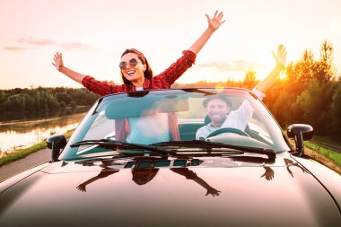 Arabayla seyahat etmek - aşık mutlu bir çift gün batımında Cabriolet arabasıyla gider