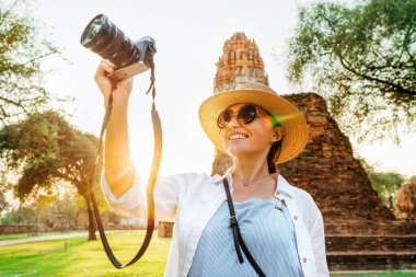 Antik Ayutthaya şehrinin sokaklarında yürüyen, kompakt kamerayla antik harabelerin fotoğrafını çeken turist kadın.