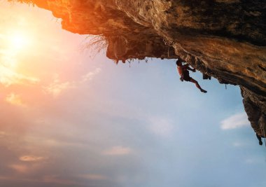 Atletik Adam, gökyüzü arka planında renkli bir günbatımı olan kayanın tepesine tırmanıyor. 