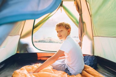 Çocuk kamp çadırında dinleniyor ve dağ vadisinde gün batımının tadını çıkarıyor.