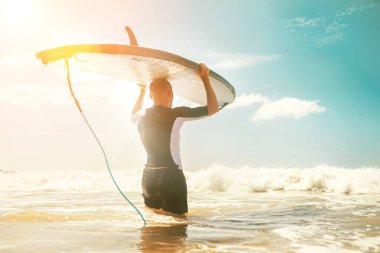 Genç sörfçü sörf tahtasını alıp dalgalara doğru uzun sörf tahtasıyla geliyor. Etkin tatil harcama kavramı. 
