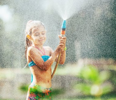Şirin küçük kız hortumdan kendine su serpti, yağmur yağdırdı. Sıcak yaz günleri için zevk.