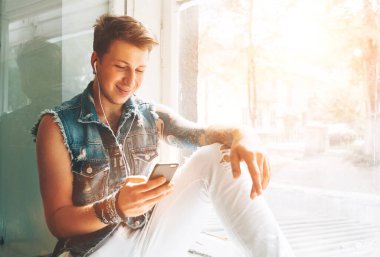 Genç adam kulaklık ve akıllı telefonla pencere kenarında oturan müziği dinle.