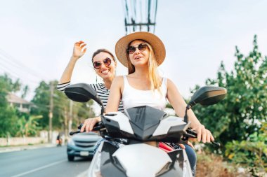 Mutlu gülümseyen kızlar Asyalı trafiğinde motosikletle geziyorlar.