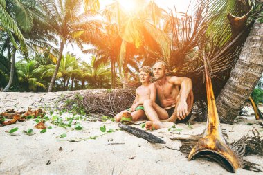Baba ve oğul kendi yaptıkları kulübede oturup Robinzone gibi oynuyorlar.