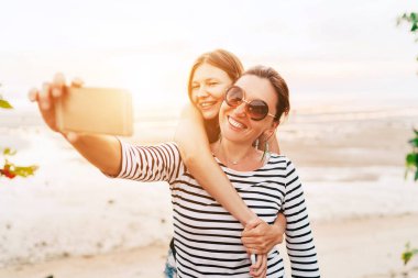 İki Kafkasyalı kız arkadaş deniz kenarında akıllı telefon kullanarak selfie çekiyorlar. Dikkatsiz tatil konsepti resmi.