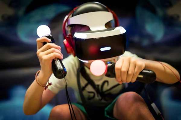 Young teenager boy using a Virtual reality headset with goggles and hands motion controllers in playing game zone. Modern technologies concept image.