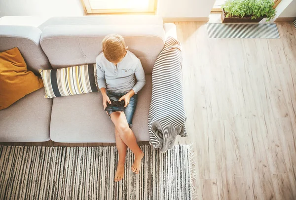 Junge Sitzt Auf Sofa Und Spielt Mit Smartphone Und Gamepad — Stockfoto