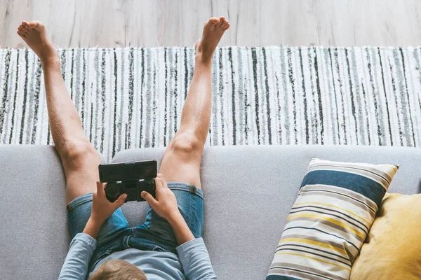 Junge Sitzt Auf Sofa Und Spielt Mit Smartphone Und Gamepad — Stockfoto