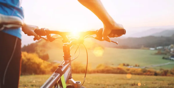 自転車を持つ男は丘の上に滞在し 夕日を楽しんでいます 自転車のハンドルの男の手を閉じる画像 — ストック写真