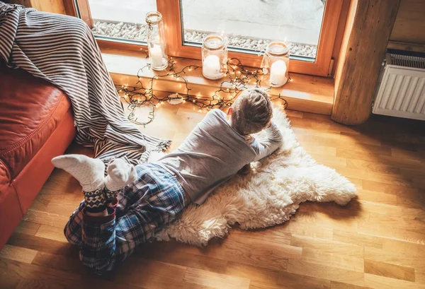 男孩躺在羊皮地板上 在舒适的家庭环境中凝视着窗外 温馨家庭概念形象的宁静时刻 — 图库照片