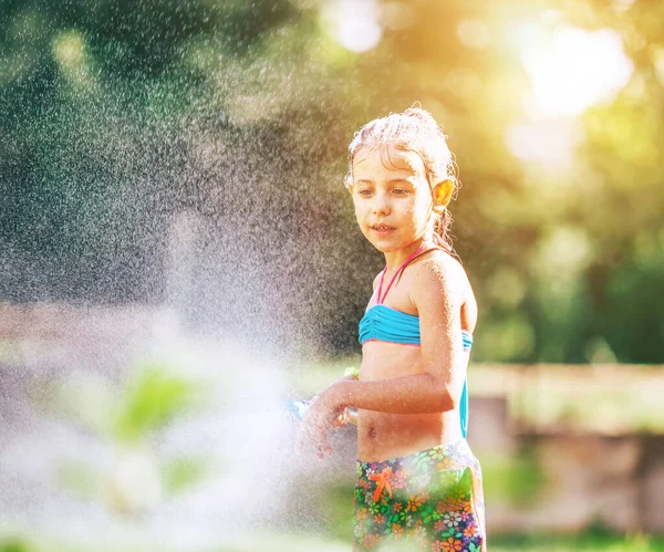 かわいい女の子はホースから自分のために水を振りかける 雨が降ります 暑い夏の日の喜び 不注意な子供時代のコンセプトイメージ — ストック写真