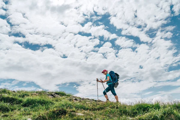 女背包客用明亮的云彩背景的远足杆爬上山顶 按运动人士概念分列的积极度假开支水平形象 — 图库照片