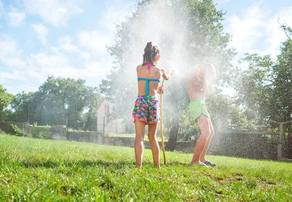 Sister and brother playing with watering hose in hot summer afternoon on