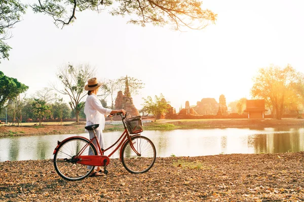 在泰国的Ayutthaya历史公园附近 年轻的女游客身穿浅色夏装 头戴浅色帽子 每天清晨骑着自行车散步 在古老的废墟前 晨曦笼罩着晨曦 — 图库照片