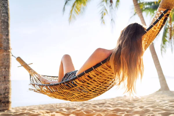 金发女人在沙滩上的棕榈树间挂着吊床放松自己 — 图库照片