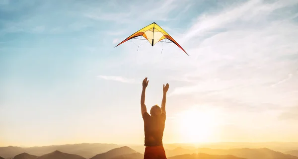 男は高い山の上の日没の空に明るい凧を飛ぶようになった 成功したスタートアップコンセプトイメージ — ストック写真