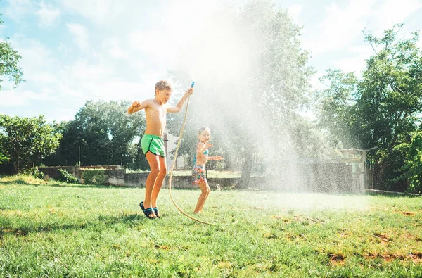 炎炎夏日活动 快乐的小女孩跳入水底 哥哥把她从花园的软管里浇了出来 — 图库照片