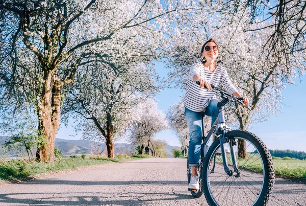 Szczęśliwa Uśmiechnięta Kobieta Jeździ Rowerem Wiejskiej Drodze Pod Kwitnącymi Drzewami — Zdjęcie stockowe