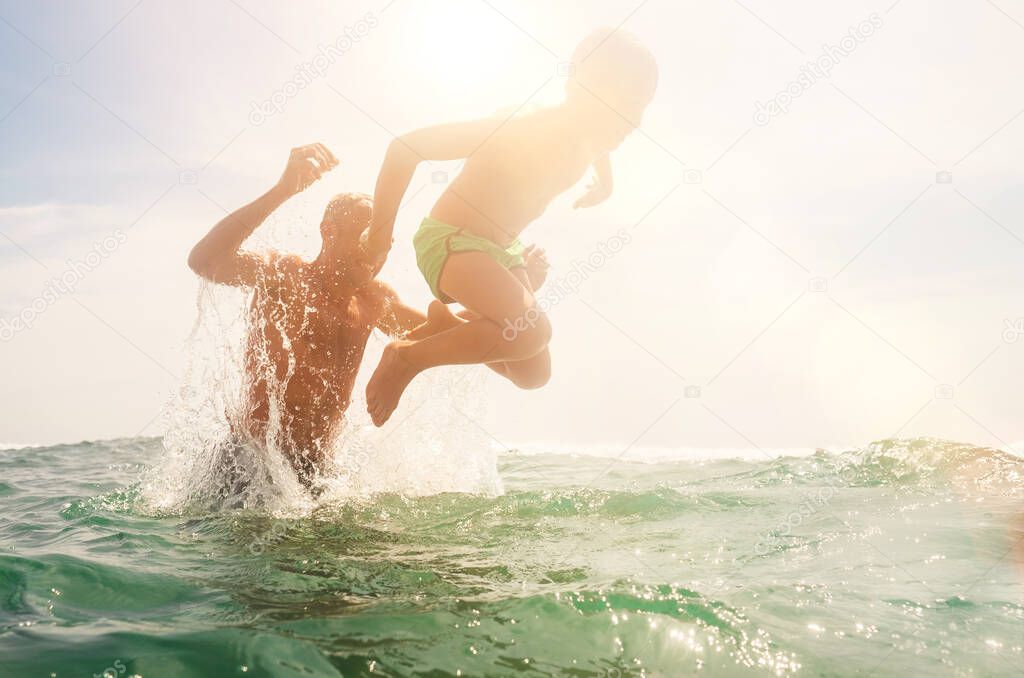 Father and son playing in water together. They cheerfully laughing when father throwing boy into sea waves water.