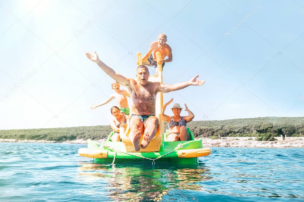 Happy family grandfather sliding down with hands up on floating Playground slide Catamaran as his multigeneration family enjoying sea trip as they have summer season vacation
