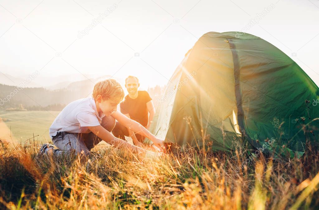 Father learn his son set up camping tent on sunset forest glade