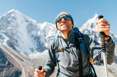 Taboche 6495m ve Cholatse 6440 m arkaplanda yürüyüş direkleriyle gülümseyen Yürüyüşçü 'nün portresi, güneş gözlüklerini koruyan UV. Everest Ana Kampı 'nın yürüyüş rotası boyunca dağ manzarasının keyfini çıkarıyor..