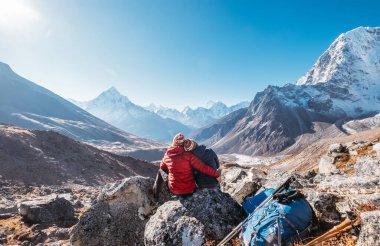 Dughla 4620 metre yakınlarındaki Everest Kampı yürüyüş rotasında birbirine sarılan çift. Sırt çantaları ve yürüyüş direklerinden ayrılan gezginler, Ama Dablam 6812 metre zirvesi ve Tobuche 6495 metresiyle vadi manzarasının keyfini çıkarıyorlar.