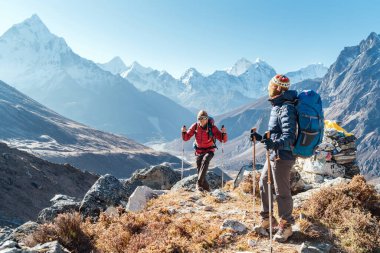 Dughla 4620 metre yakınlarındaki Everest Ana Kamp 'ı takip eden çift. Sırt çantaları taşıyan ve yürüyüş direkleri kullanan gezginler, Ama Dablam 6812 metrelik zirvesiyle vadi manzarasının keyfini çıkarıyorlar.