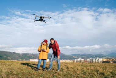 Baba ve genç çocuk sarı ceketli uzaktan kumandayla modern dijital bir drone kullanıyor. Modern teknoloji konsept imajını bozar