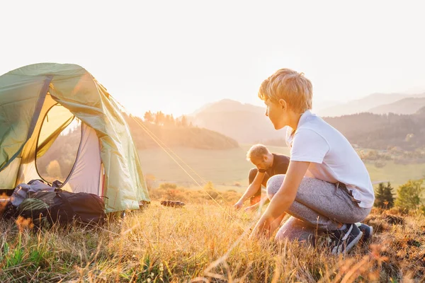 父と息子は夕日の山の谷でテントキャンプを設定します — ストック写真