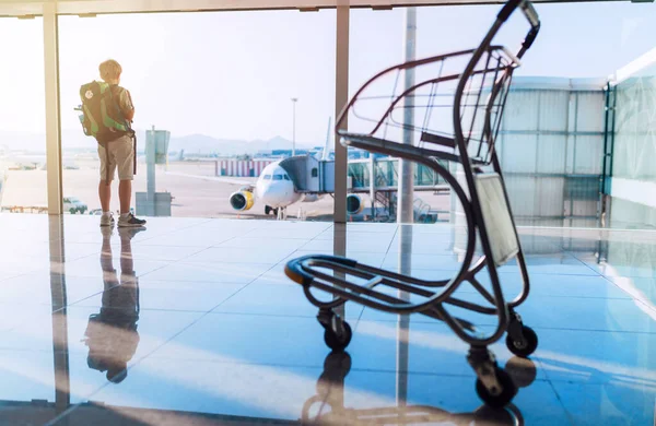 単独でバックパッカーの旅行者カミノ サンティアゴ巡礼少年は 空港ターミナルの待合室に立って 窓の後ろの飛行のために準備された航空機に搭乗するのを待ちます — ストック写真
