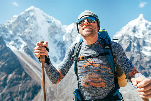 Portrait of smiling Hiker man on Taboche 6495m and Cholatse 6440m peaks background with trekking poles, UV protecting sunglasses. He enjoying mountain views during Everest Base Camp trekking route.