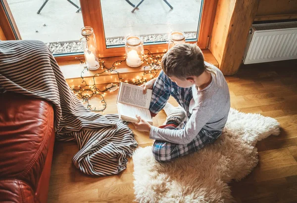 居心地の良い家庭的な雰囲気の中で羊の皮の上の床の上に少年読書本 居心地の良い家庭のコンセプトイメージの静かな瞬間 — ストック写真