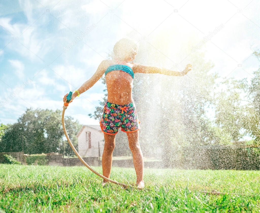 Cute little girl refresh herself from garden watering hose