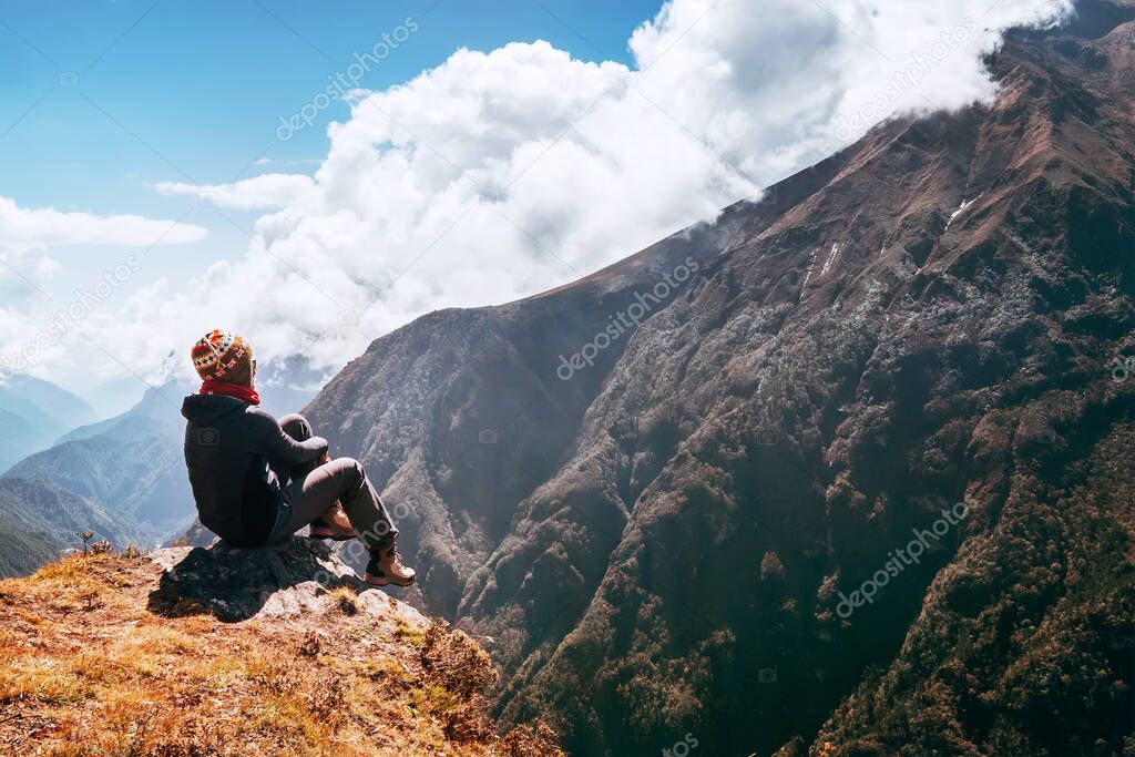 Young female hiker backpacker sitting on the peak edge and enjoying mountains view valley during high altitude Everest Base Camp (EBC) trekking route near Phortse,Nepal. Active vacations concept image