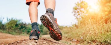 Trek bot teknesi yaz mevsiminde dağdaki kirli patikada yürüyüş botlarıyla gezgin ayaklarını kapatıyor. Arka plan görüntüsü.