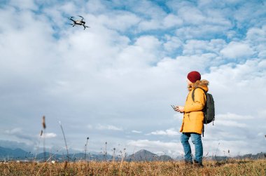 Sarı ceketli genç çocuk uzaktan kumandayla modern dijital bir drone kullanıyor.